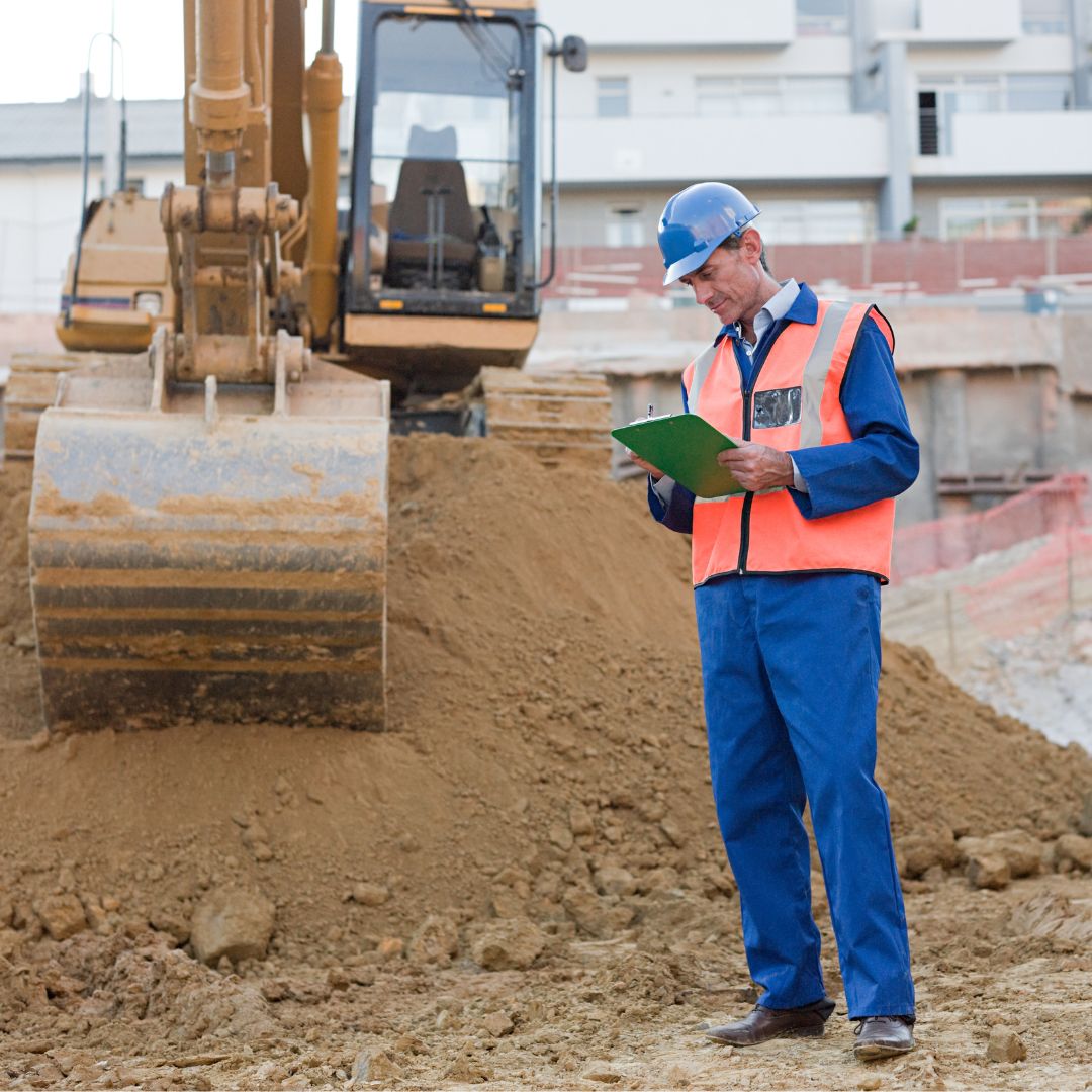 homme regardant un carnet devant un tractopelle